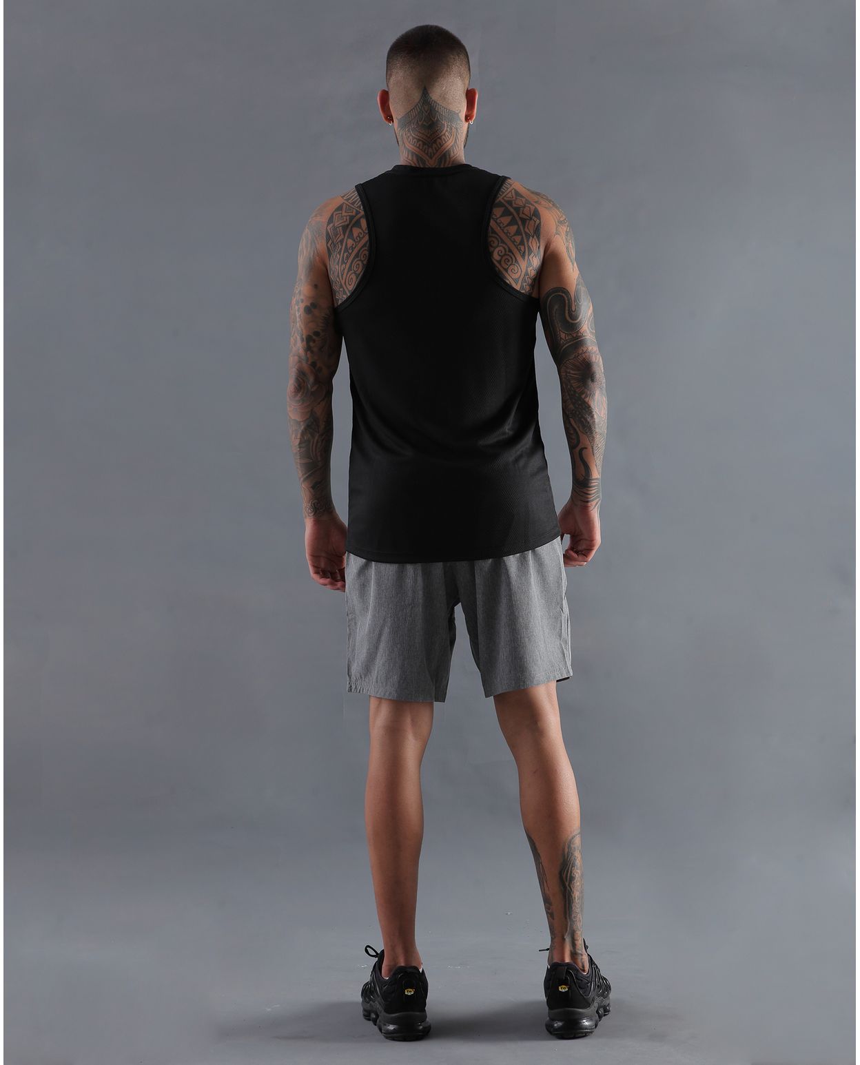 modelo con camiseta basica color negra y pantaloneta deportiva color gris para hombre cuerpo completo parte trasera