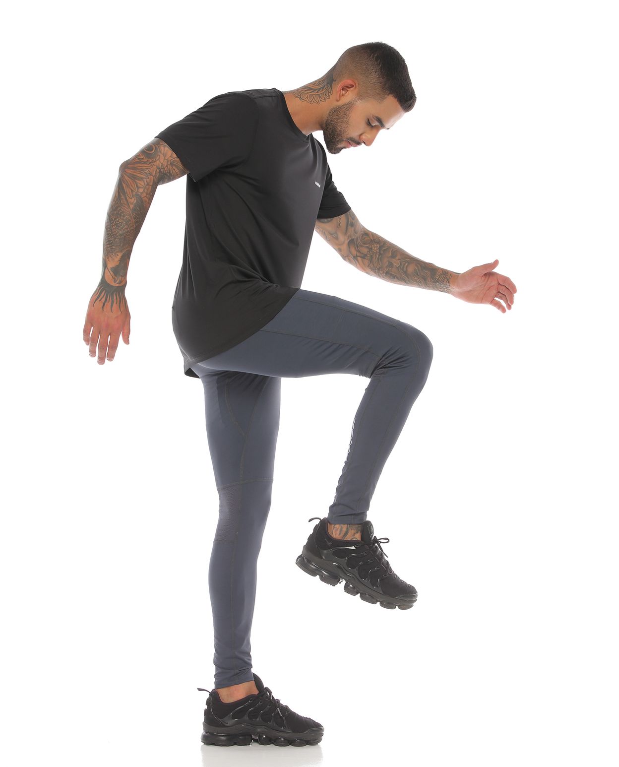 modelo con licra deportiva color gris oscuro y camiseta deportiva color negro para hombre cuerpo completo parte lateral derecha