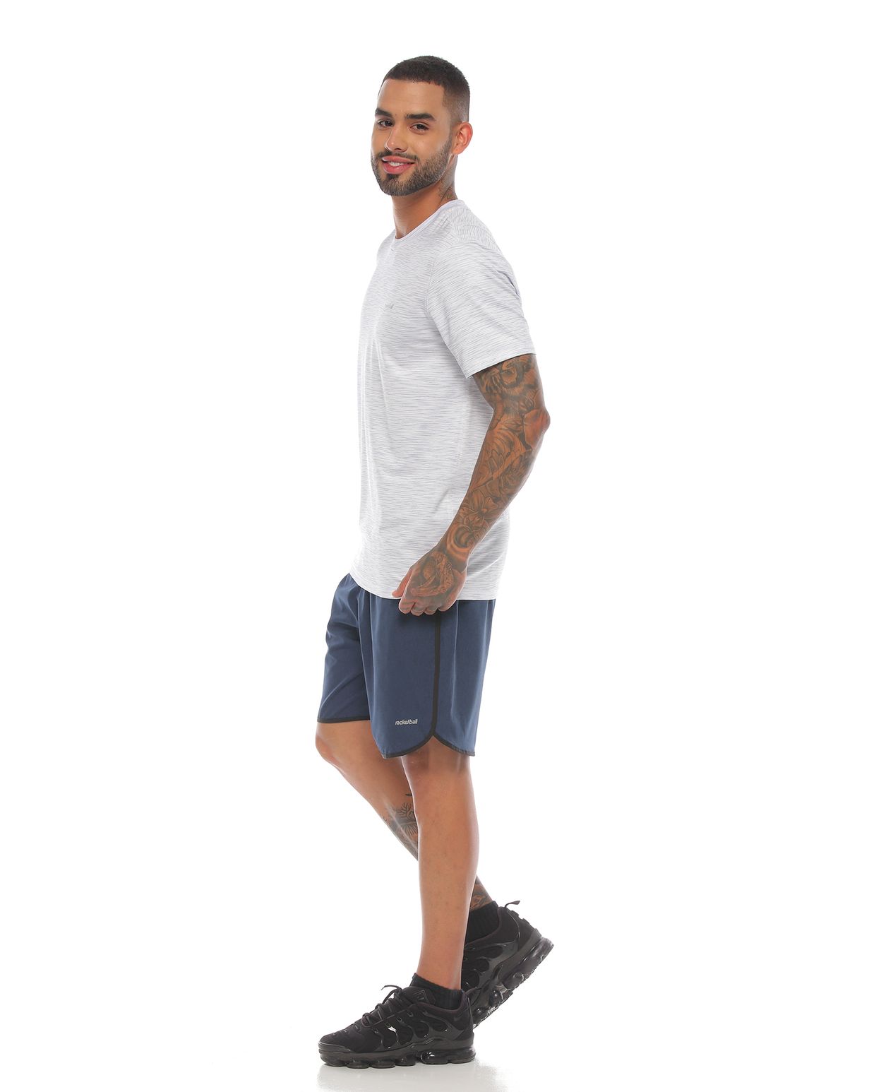 modelo con pantaloneta deportiva color petroleo negro y camiseta manga corta deportiva color blanca para hombre cuerpo completo parte lateral izquierda