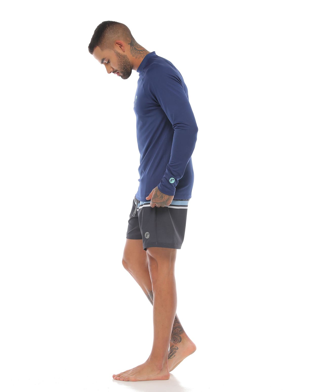 modelo con camibuso proteccion uv color azul oscuro y pantaloneta de playa color gris para hombre cuerpo completo parte lateral derecha